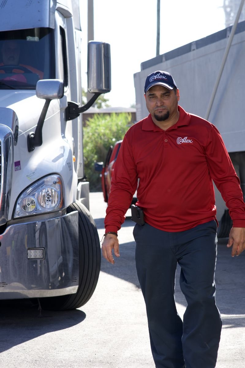 Alex Truck Tire team member in the red company polo walking past a semi-truck at the Medley shop